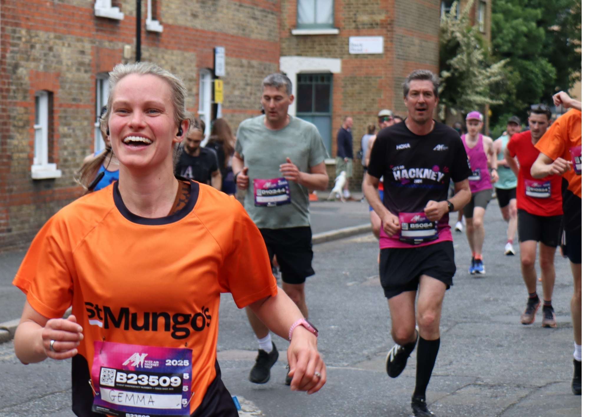 A group of runners with focus on a female runner wearing the orange St Mungo's tee shirt and laughing while running.