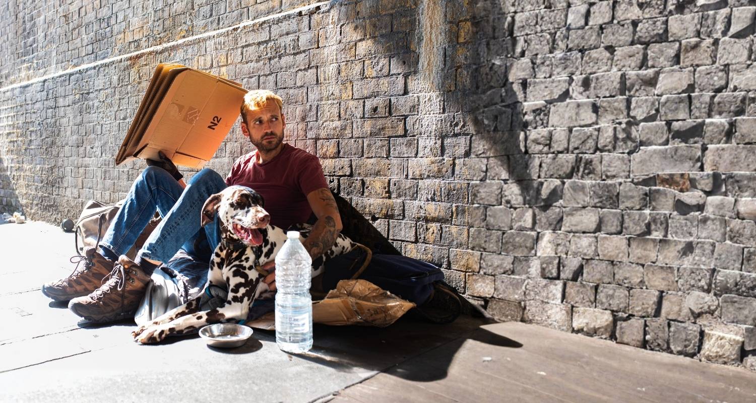 A man and dog on the street experiencing homelessness trying to shelter from the heat.