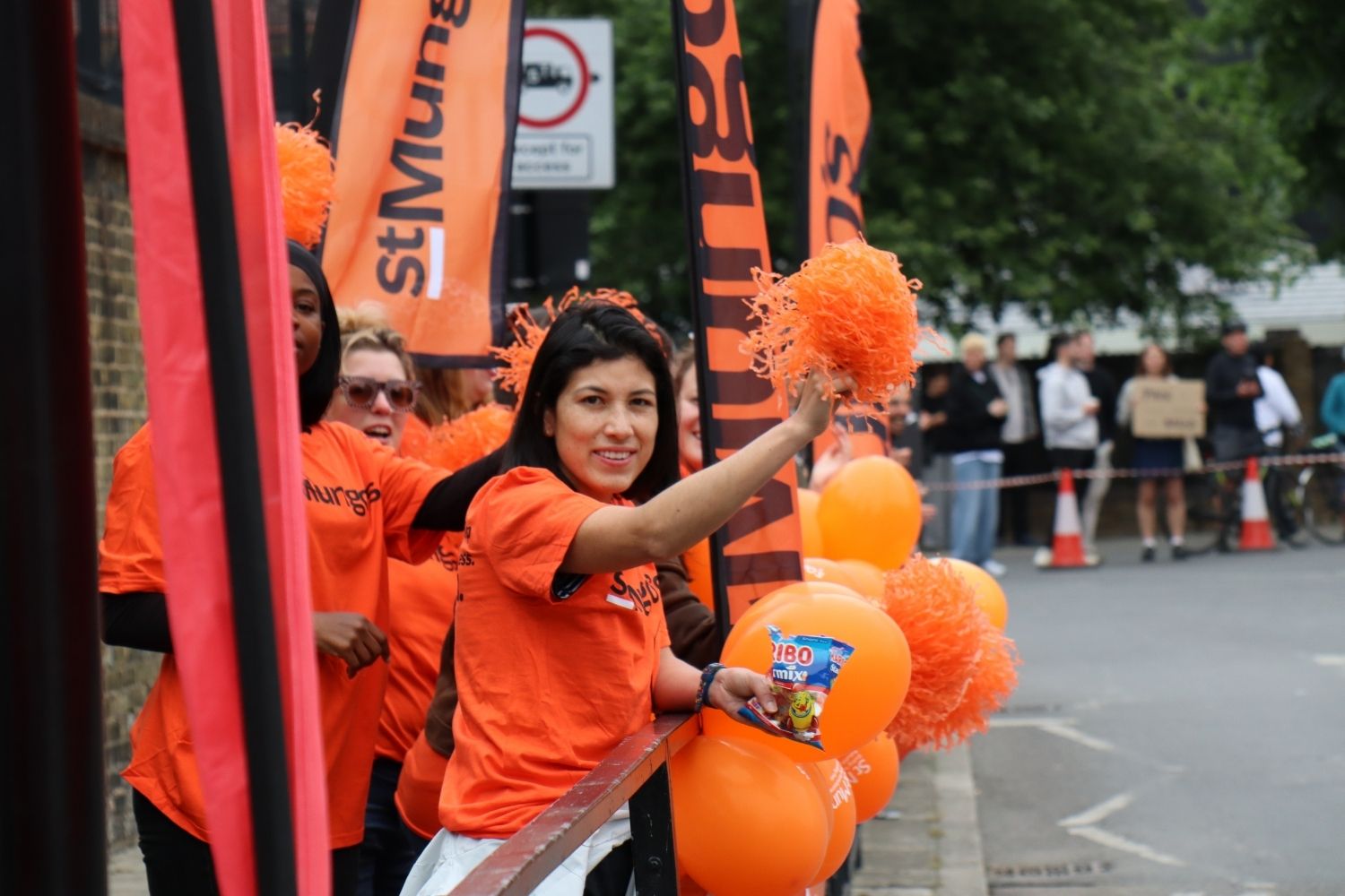 A group of cheerers in a corner on the road, wearing Mungo's branded tee shirt and celebrating with other blurred by lookers showing in the background.