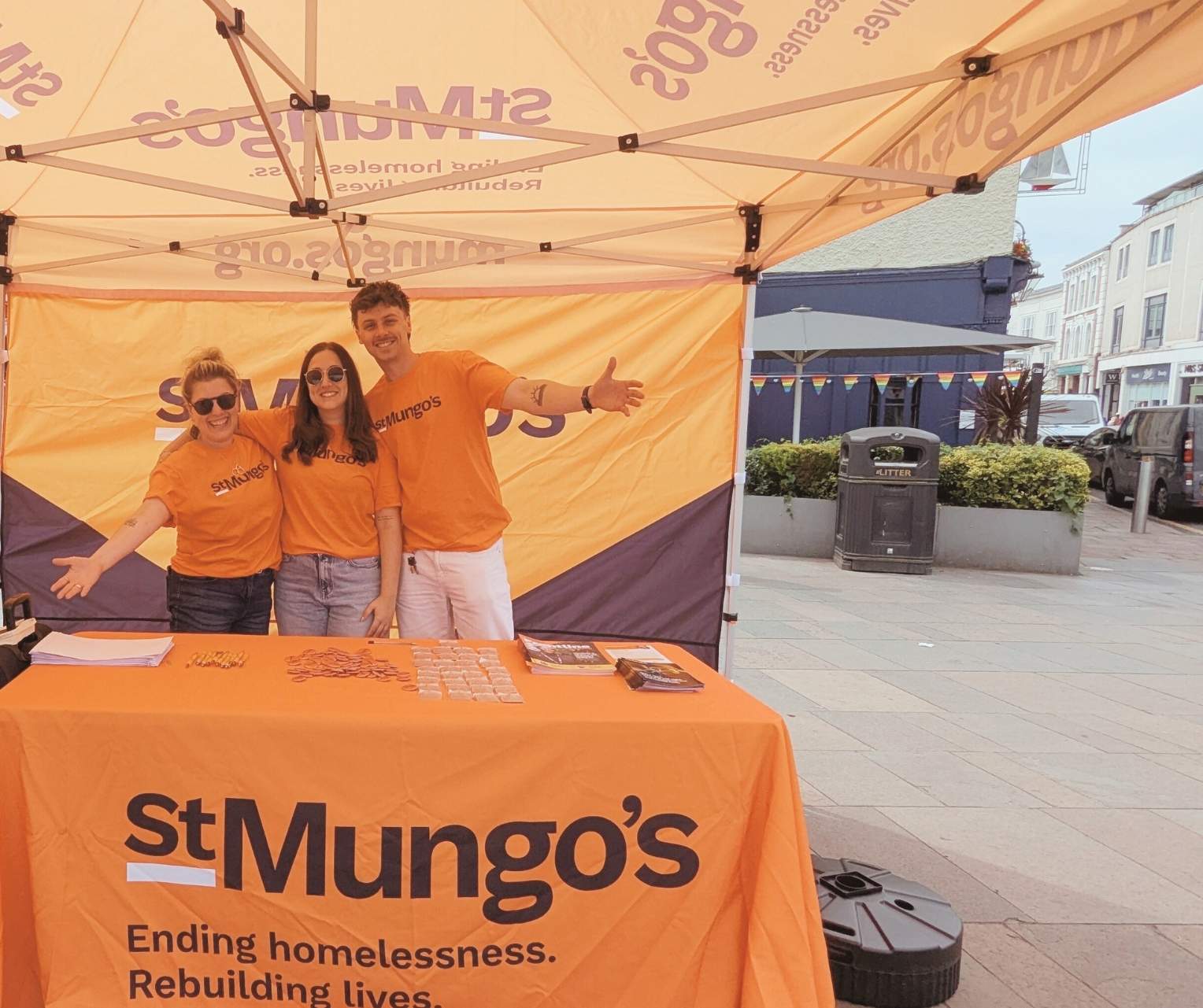 3 St Mungo's team members behind a table decorated with a St mungo's branded banner.