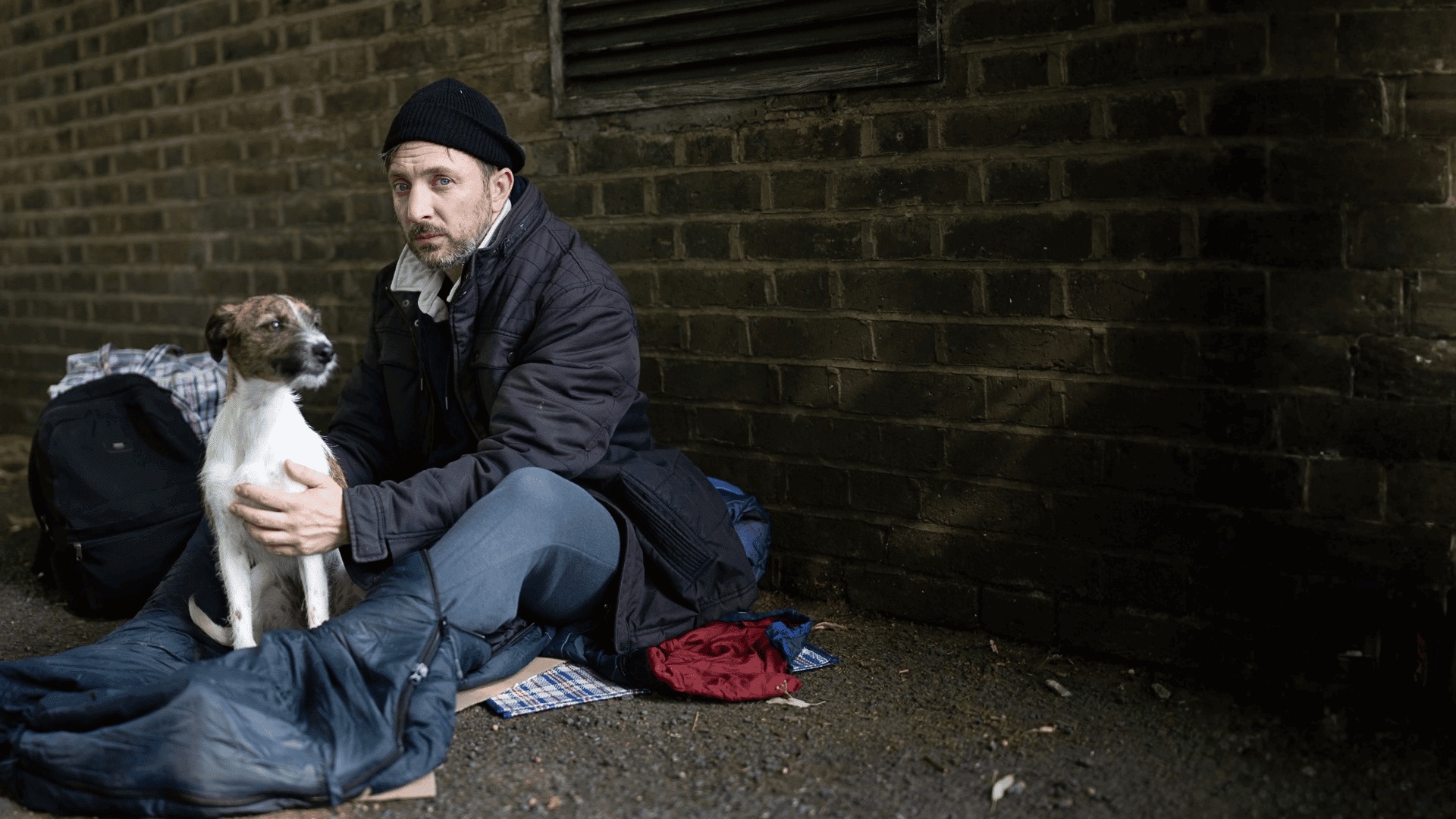 Man and dog sat outside, wearing warm clothes. 