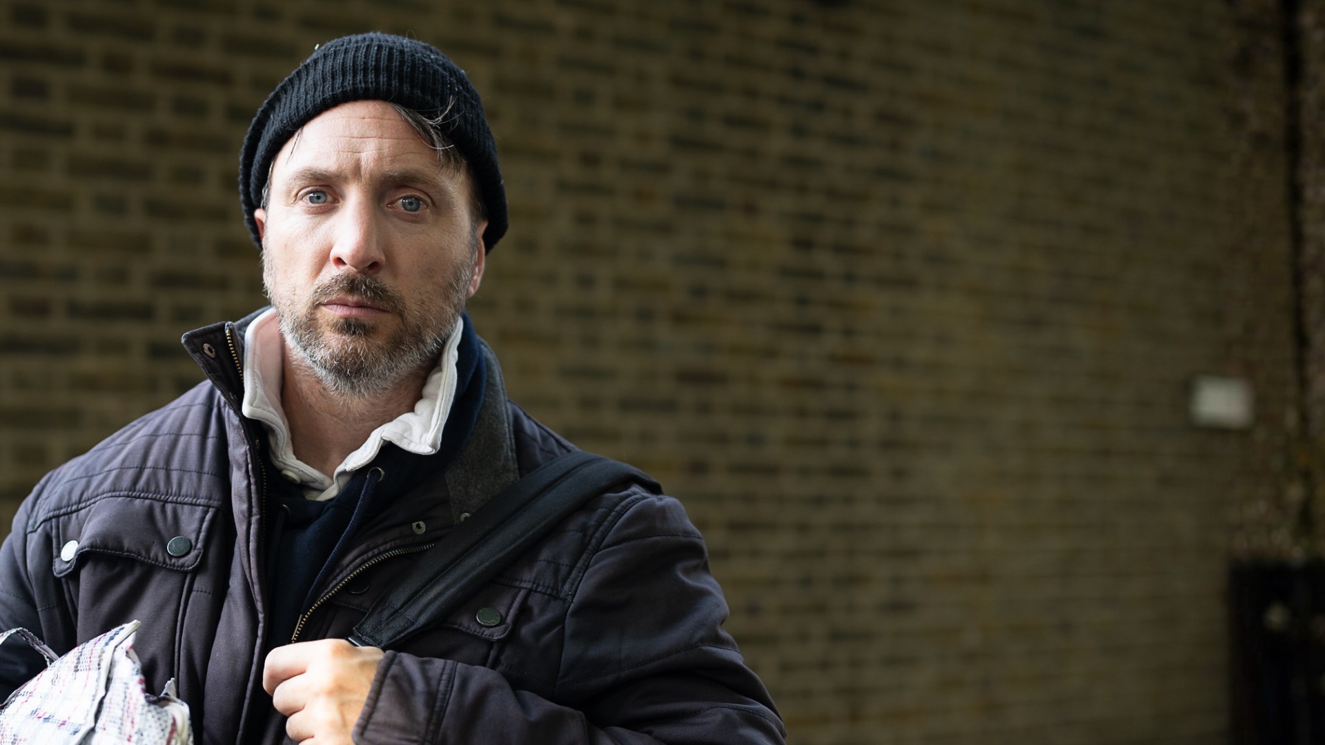 Man outside, wearing warm clothes and carrying bags