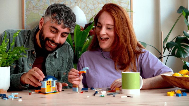 Two Adults sitting at a kitchen table building the Mini Build house together having fun.